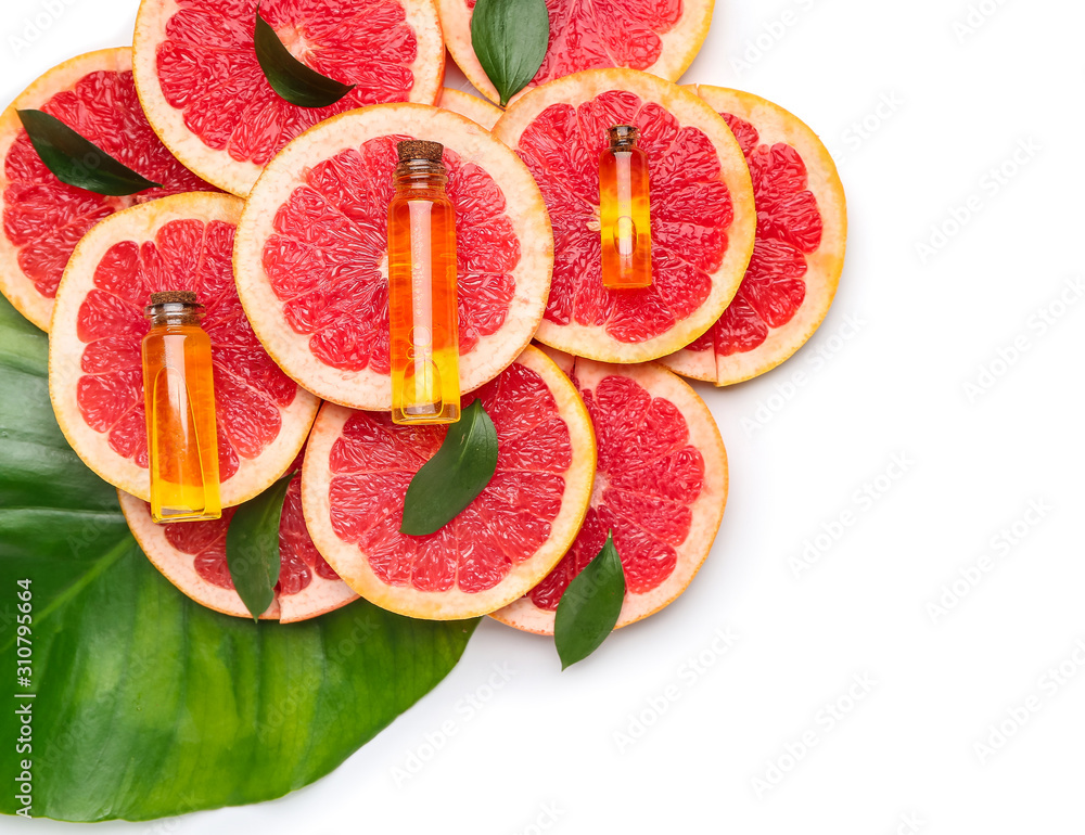 Bottles of essential oil and grapefruit slices on white background