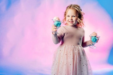 Little girl in a beige dress holds 2 balls of ice cream in her hands on a blue background and smiles