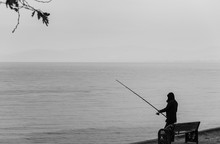 Silhouette Of Fisherman At Sunset. Black And White Seascape. Silhouette Of People As Blots. Monochrome Photo Suitable For Dramatic Studies. Free Space For Writing.