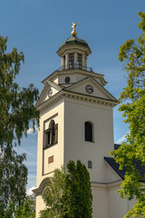 Poster - White church tower in evening sunlight surrounded by green foliage