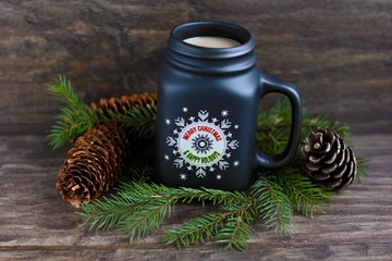 Wall Mural - Christmas, new year concept with mug of hot coffee with milk against rustic wooden background with spruce branches and cones. Selective focus.