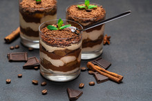 Classic tiramisu dessert in a glass cup and pieces of chocolate on dark concrete background
