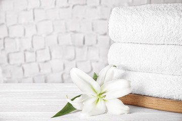 Stack of clean bath towels and beautiful flower on white wooden table. Space for text