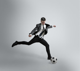 Dream about the biggest win in life. Man in office clothes traines in football or soccer with ball on grey background. Unusual look for businessman in motion, action. Sport, healthy lifestyle.