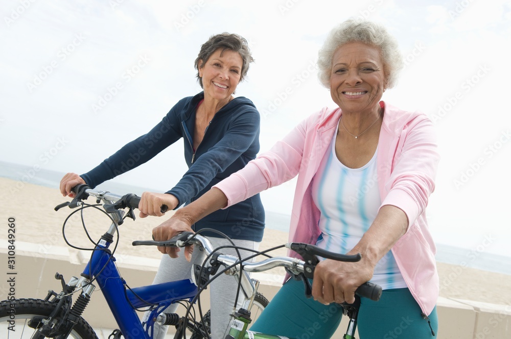 Portrait of happy senior multiethnic female friends riding bicycles together - obrazy, fototapety, plakaty 