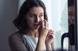 © nenetus - Sad young woman crying while looking through the window at home.