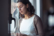 © nenetus - Sad young woman crying while looking through the window at home.