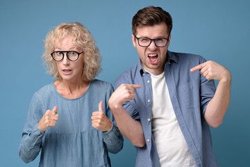 Displeased caucasian man and woman, dressed in casual clothes, pointing with index fingers saying are you blaming us for your mistake.