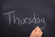 Woman's Hand Writing The Day Of The Week On A Blackboard With White Chalk, Thursday