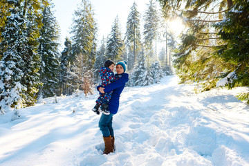 Happy mother and child boy having fun, walking in snowy winter forest. Family spend time together outdoors. Mom with little kid playing with snow and smiling in park. Christmas holiday with children.