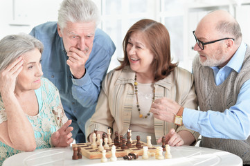 Poster - Close up portrait of two senior couples sitting at table and playing chess