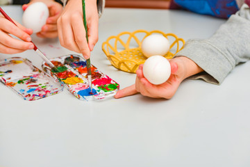 Children paint eggs for Easter, a boy and a girl paint eggs with watercolors with a small brush.