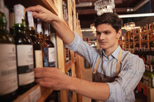 Cheerful Male Sommelier Organizing Bottle On The Shelves Of His Wine Store