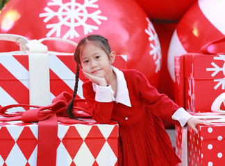 Wall Mural - Beautiful little girl in red dress poses with big gift box in winter season and happy new year festival against christmas background.