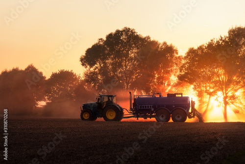 Tractor fertilizing agricultural field at sunset. Agriculture