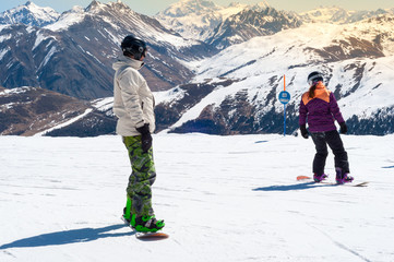 experienced snowboard instructor giving ride lesson to young woman. sunny day in the alpine resort, 