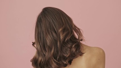 back view of half-naked woman is shaking her hair with hands isolated over pink background