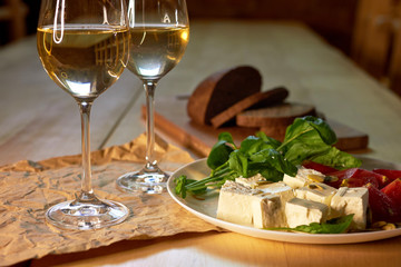 Two glasses of white wine, plate with cheese and tomatoes and a few pieces of bread on a wooden table in a wine cellar restaurant