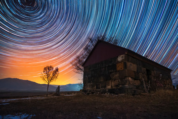 Wall Mural - Beautiful night landscape, small church and star trails. The colorful star trails on the sky with orientation on the north star. Night time lapse photography.