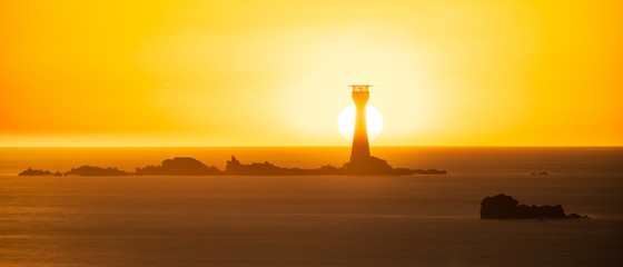 Wall Mural - Breathtaking shot of the sun shining over a lighthouse in the middle of the sea in Guernsey