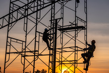 Silhouette Of Engineer And Construction Team Working Safely On Scaffolding On High Rise Building. Over Blurred Background Sunset Pastel For Industry Background With Light Fair
