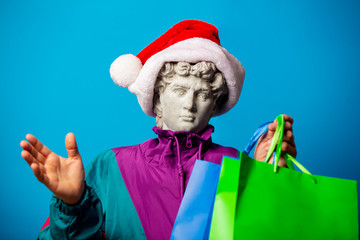 Wall Mural - antique statue dressed in trendy clothes of the nineties and Santa Claus hat with shopping bags