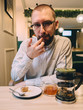 © paulzhuk - Man with beard and glasses in cafe eats dessert tea