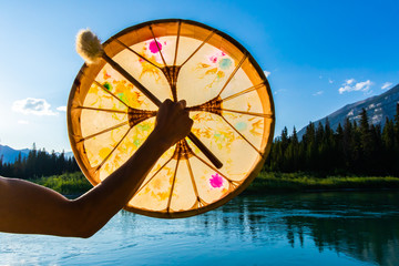 A close up shot on the arm of a spiritual person holding a mystical native drum against nature, used in alternative healing and powwow ceremony