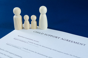 Printed child support agreement with man, woman and children wooden figures in a conceptual image for financial child support. Over blue background.