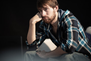 Sad young man sitting on the couch looking into space