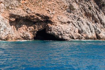 Photo of a cave, looking dark and cold, in a rocky sea coast on sunny summer day.