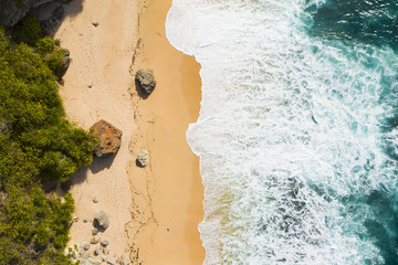 Wall Mural - View from above, stunning aerial view of a rocky shore with a beautiful beach bathed by a rough sea during sunset, Nyang Nyang Beach (Pantai Nyang Nyang), South Bali, Indonesia.