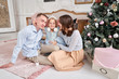 Loving family. Mom and dad hugging little daughter . Parents and baby child having fun near Christmas tree and white fireplace indoors. Merry Christmas and Happy New Year. Cheerful pretty people.