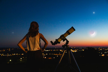 Wall Mural - astronomer with a telescope watching at the stars and moon with blurred city lights in the backgroun
