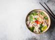 Traditional Vietnamese soup- pho ga in bowl with chicken and rice noodles, mint and cilantro, red onion, chili, bean sprouts and lime on grey background. Asian food. Copy space. Top view