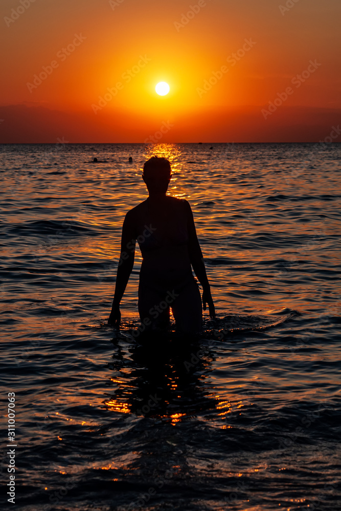 Young woman walking on water at sunset. Sunset and silhouette of a ...