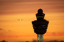 Amsterdam Schiphol International Airport Control Tower With A Plane Landing In The Background During Sunset.