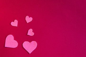 Pink felt hearts on a red background. St. Valentine's Day and romance concept. Top view, flat lay. Copy space.