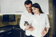 © hetmanstock2 - Cute couple on a kitchen. Pretty brunette in a white shirt. Man and woman use the phone