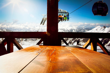 Canvas Print - Wooden table background of free space and winter landscape of mountains.Ski time and blue sky with sun. 