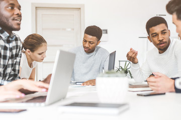 Wall Mural - A team of young office workers, businessmen with laptop working at the table, communicating together in an office. Corporate businessteam and manager in a meeting. coworking.