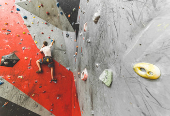 Wall Mural - Sportsman climber moving up on steep rock, climbing on artificial wall indoors. Extreme sports and bouldering concept