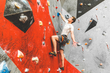 Wall Mural - Sportsman climber moving up on steep rock, climbing on artificial wall indoors. Extreme sports and bouldering concept