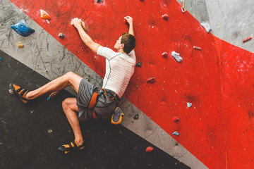 Wall Mural - Sportsman climber moving up on steep rock, climbing on artificial wall indoors. Extreme sports and bouldering concept