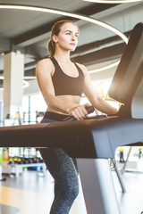 Poster - The athletic woman dressed in a black sportswear running on the treadmill in the modern gym