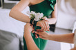 The bride helps the girlfriend to put the peony buttonhole on her hand and lace it up. Wedding boutonniere from flowers, details, scenery.