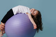 girl lies back on lilac fitness ball.