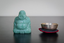 Chinese Buddha Next To A Small Singing Bowl On Dark Wood