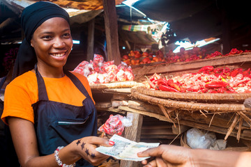 Canvas Print - young african woman selling tomatoes in a local african market collecting money from a paying customer