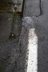 Wall Mural - Close up of rainwater running down the edge of the street and sidewalk